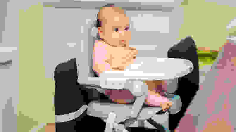 A baby sitting in a booster seat at a dining table.