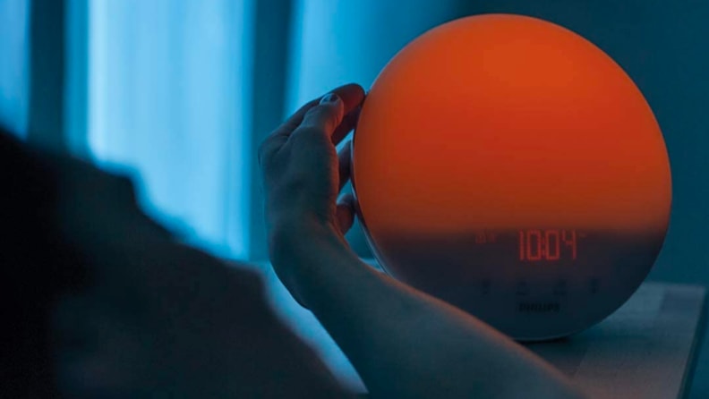 A person turns off their sunrise alarm clock.