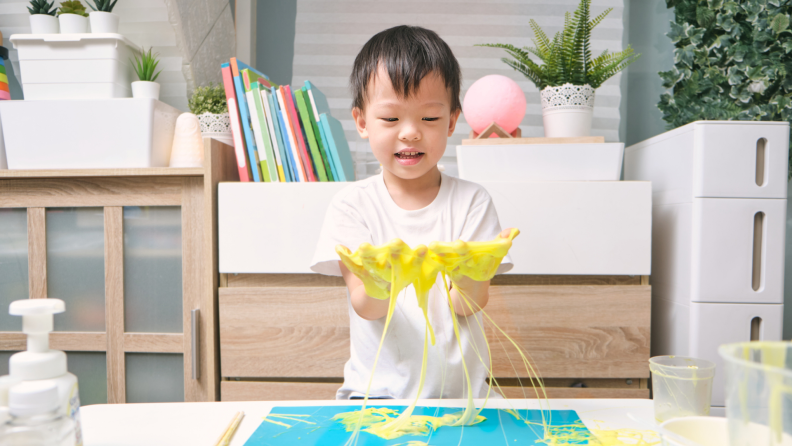 Smiling young boy having fun making yellow fluffy slime