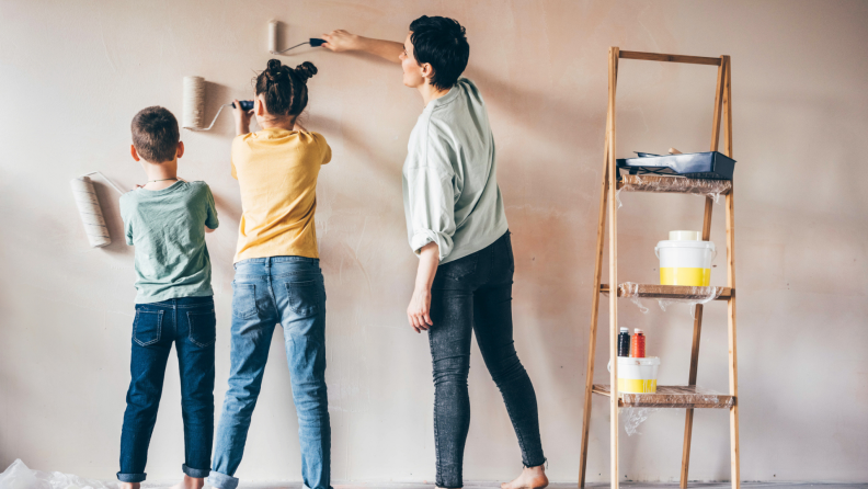 Family of three painting walls with interior paint next to a wooden ladder