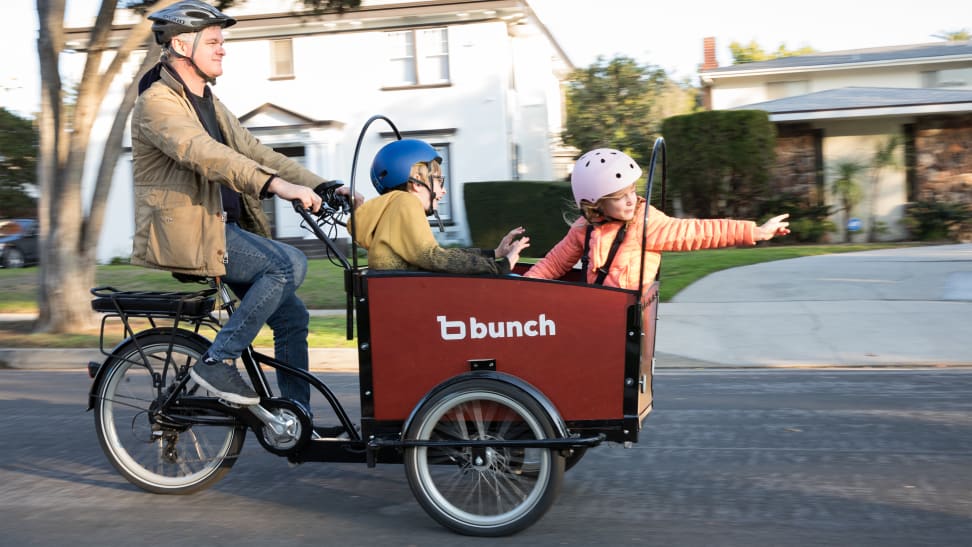 A man pedals a Bunch Bike while two kids ride in the cargo compartment