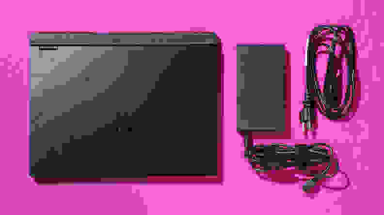 A black Acer Predator Helios Neo 14 gaming laptop with the power cable next to it, on a pink table