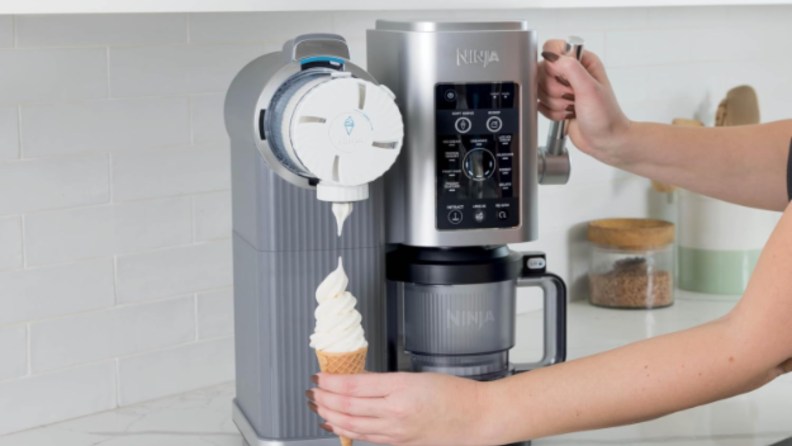 A woman's arm reaches over to use the Ninja Cream Swirl to make soft serve ice cream on a cone