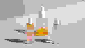 Three serum bottles with liquids in them capped with droppers stand on a light pink background.