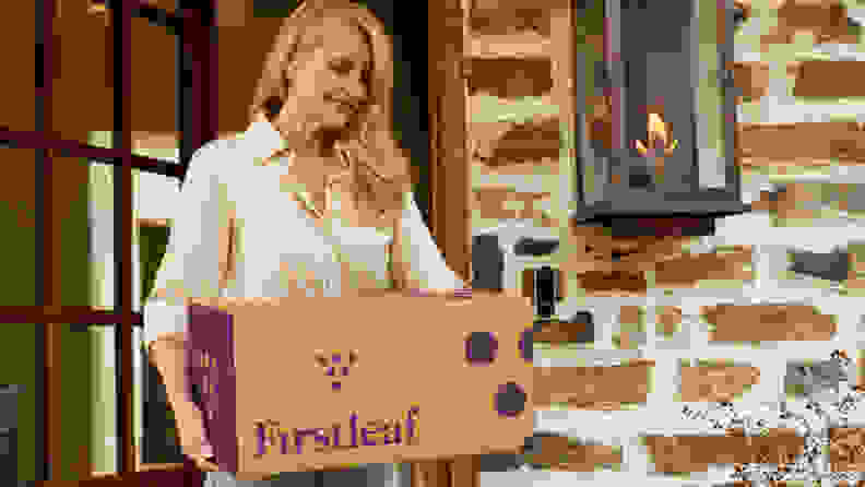 Woman holding Firstleaf box outside brick home