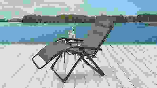 Gray antigravity lawn chair sitting on deck in front of a body of water.