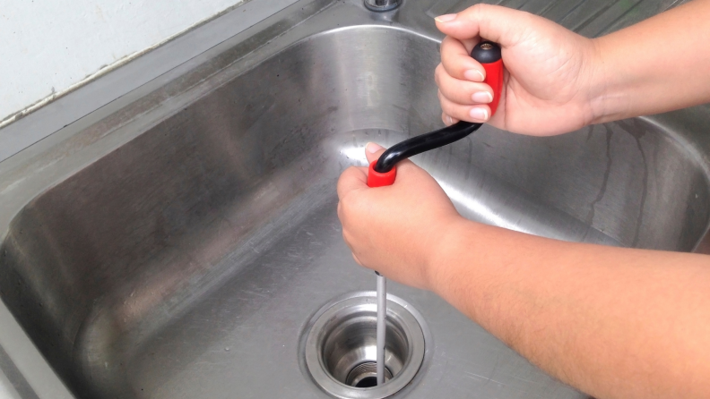 A person cleans a clogged pipe with a flexible spring drain cleaner.