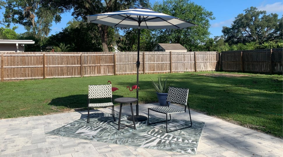 A patio set-up with an outdoor rug, two chairs, small table, and an umbrella.