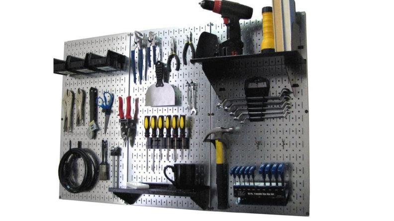 Metal pegboard with several tools attached including power tools and tool sets, along with installed shelving