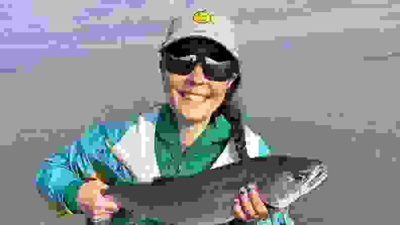 A woman holding up a freshly caught fish from the ocean.