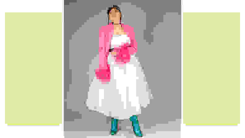 A person wearing a white tulle dress, a pink jacket with feathered sleeves, and green boots.