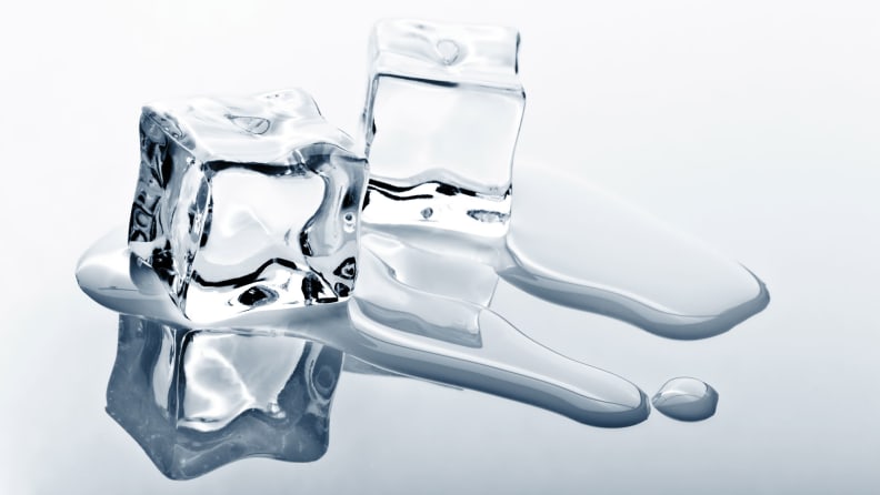 Two clear ice cubes melting on a reflective surface.