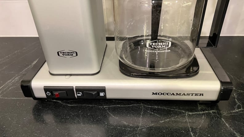 The base of the Moccamaster coffee maker on a counter, showing an empty pot and two switches.