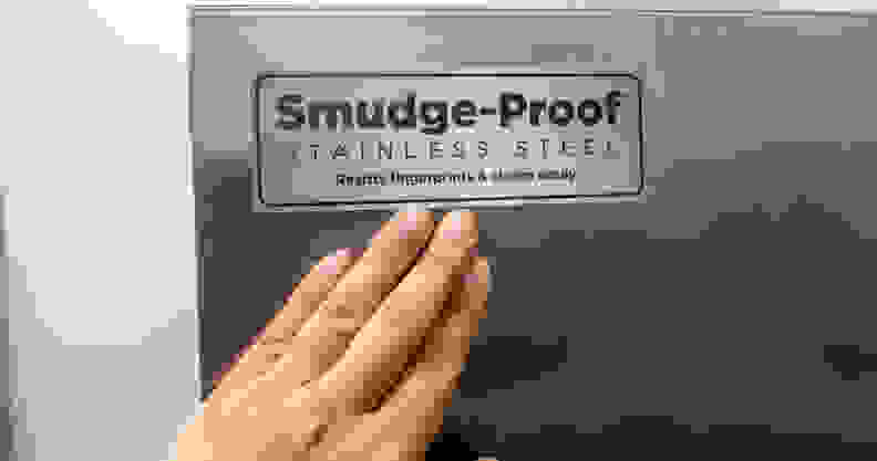 A hand reaches up to the face of the Frigidaire Gallery GRSC2352AF side-by-side refrigerator, unsuccessfully attempting to smudge it.