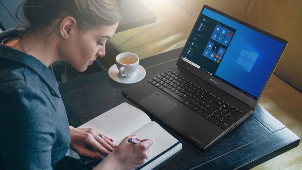 A woman works in a cafe with a dynabook satellite and a book.