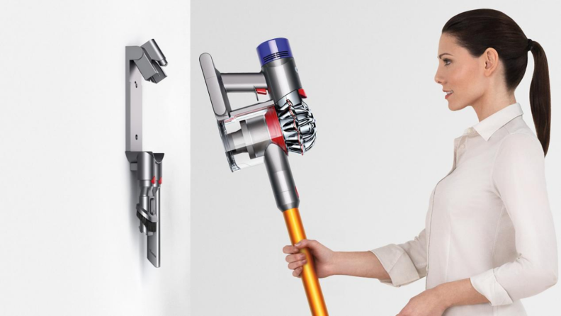 An image of a woman hanging her cordless vacuum from a wall hanger.